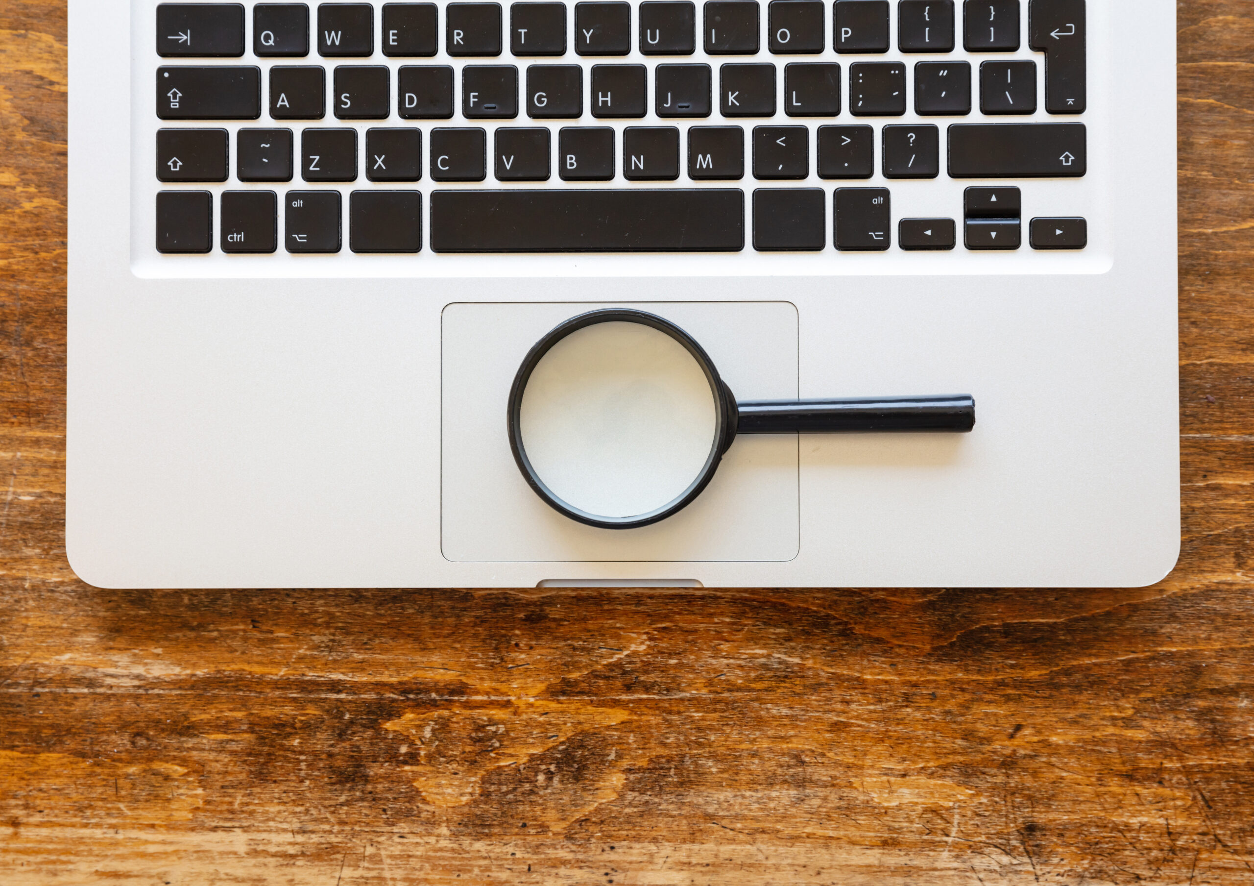 Magnifying glass on a computer laptop, wooden office desk background, top view. Search, SEO concept